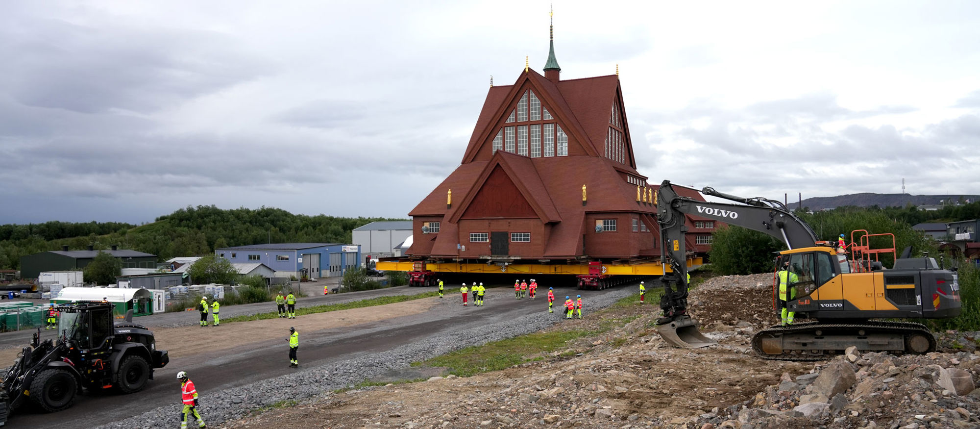 Vinterbild över Kiruna med kyrkan i förgrunden, stadens byggnader i mitten och berg mot blå himmel i bakgrunden