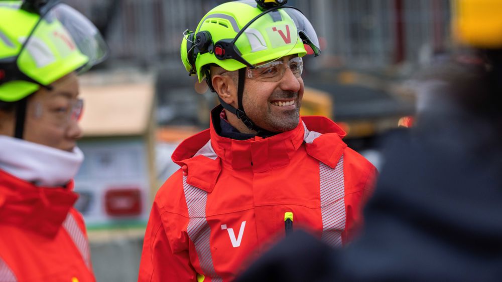 Glada personer i varselkläder och hjälmar vid ett bygge