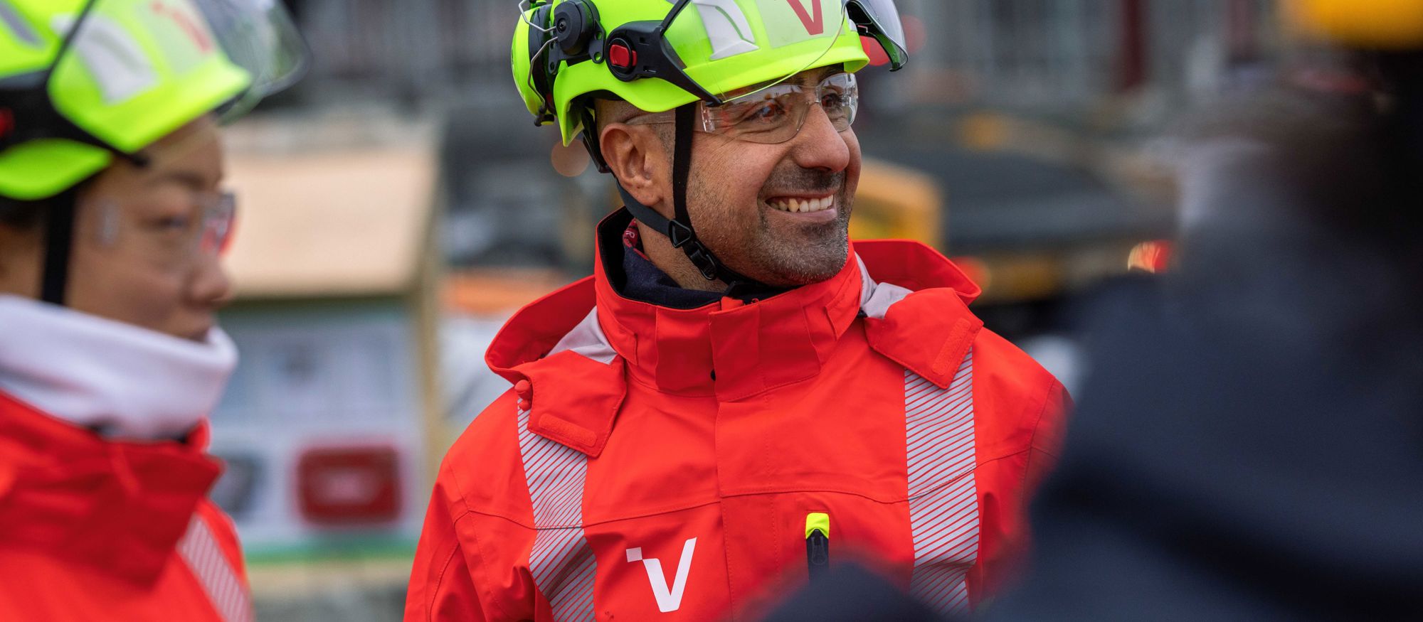Glada personer i varselkläder och hjälmar vid ett bygge