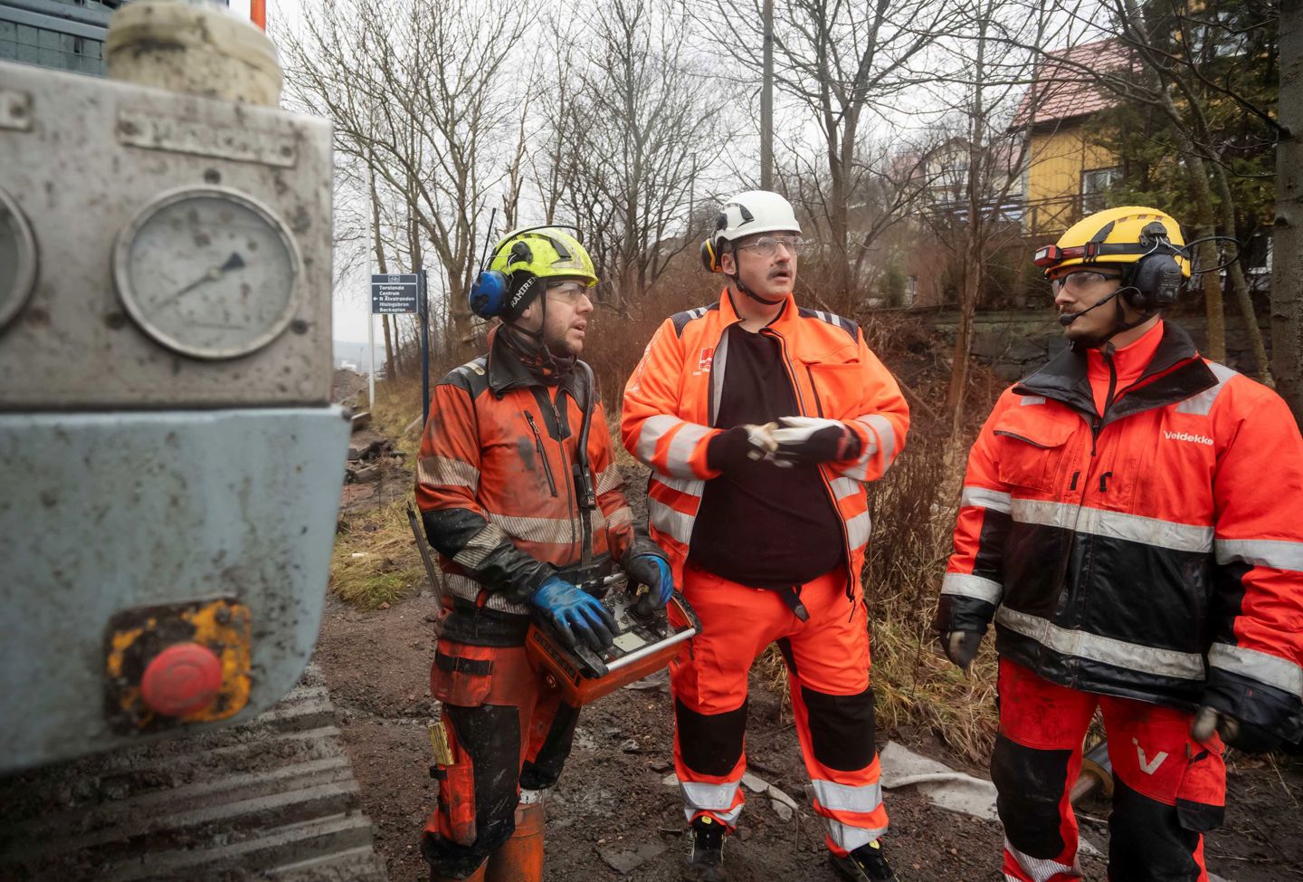Tre män på en byggarbetsplats iklädda skýddskläder och hjälmar