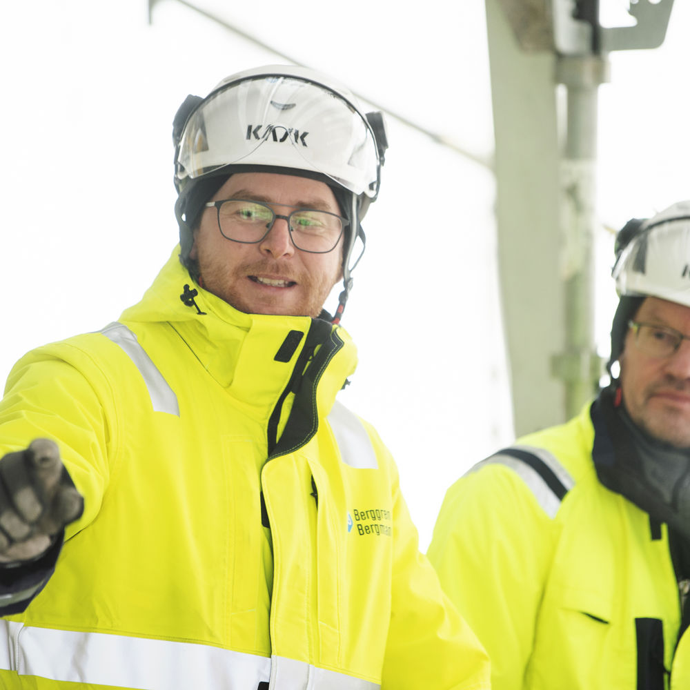 Två kollegor i hjälm och varselkläder pratar med varandra.