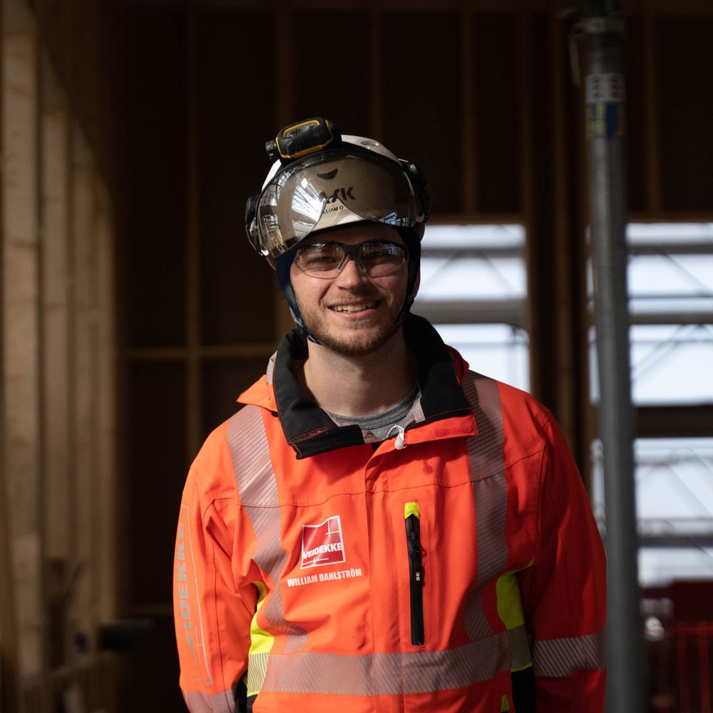 Foto av Veidekkes medarbetare William Dahlström. Står leende i varselkläder och hjälm.