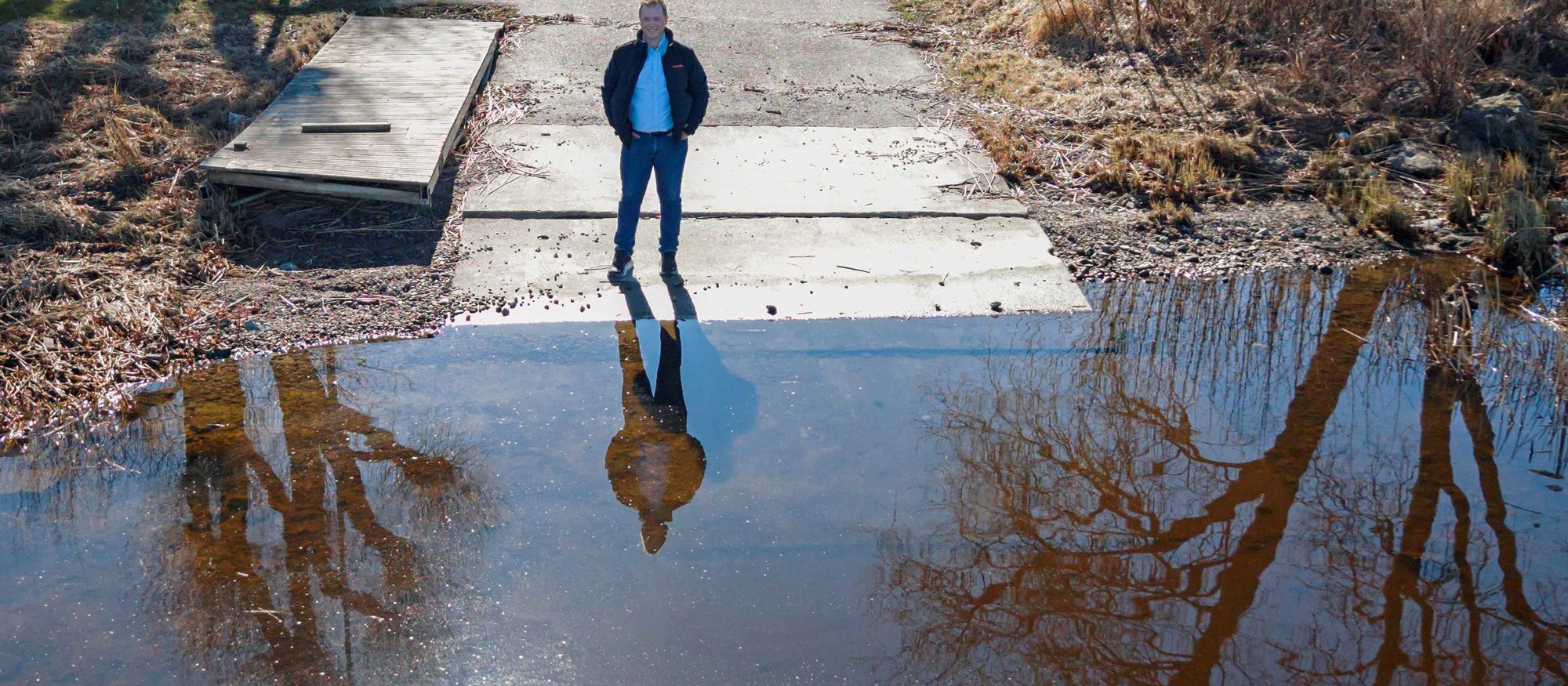 En man, Marcus Dahlberg, står vid en strandkant där solen speglar sig i vattenytan