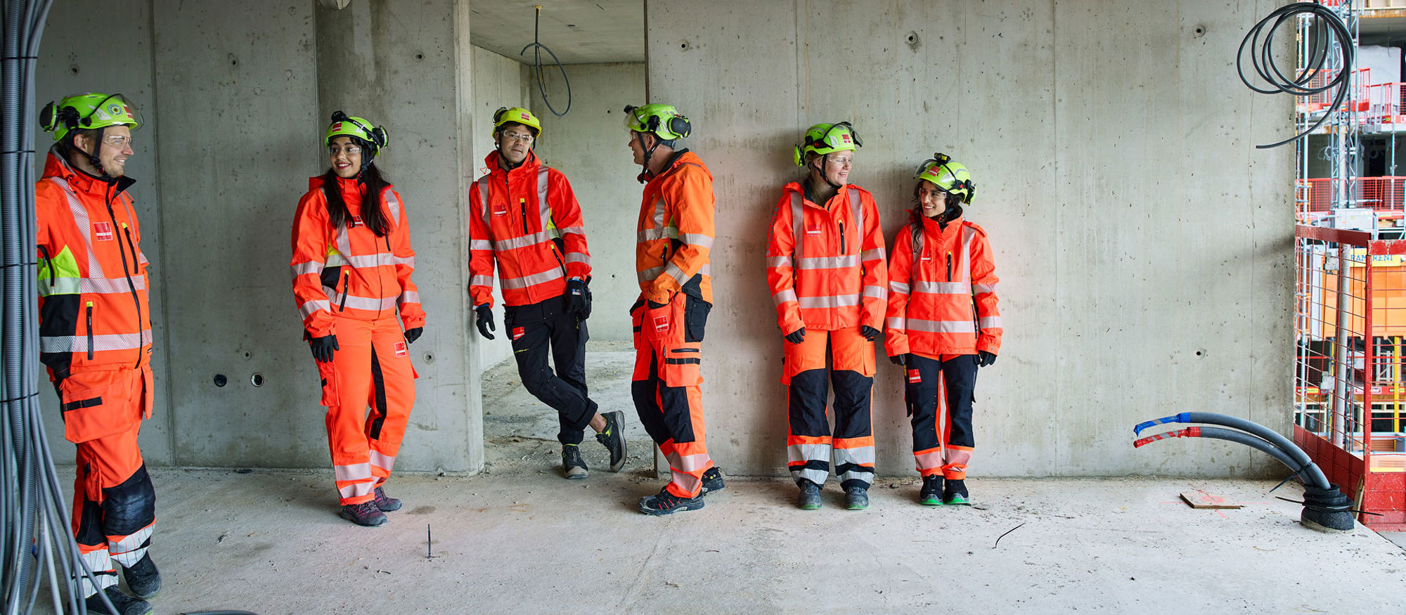 Ung kvinnlig byggarbetare i skyddsutrustning, Stella, står vid grönlysande laserpekare inomhus i ett nybuggnadsprojekt.