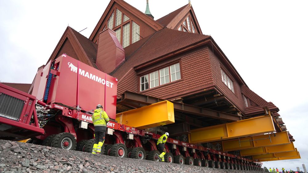 Närbild på en röd träbyggnad uppallrad på en gul trailer som rullar fram - Kiruna kyrka flyttas