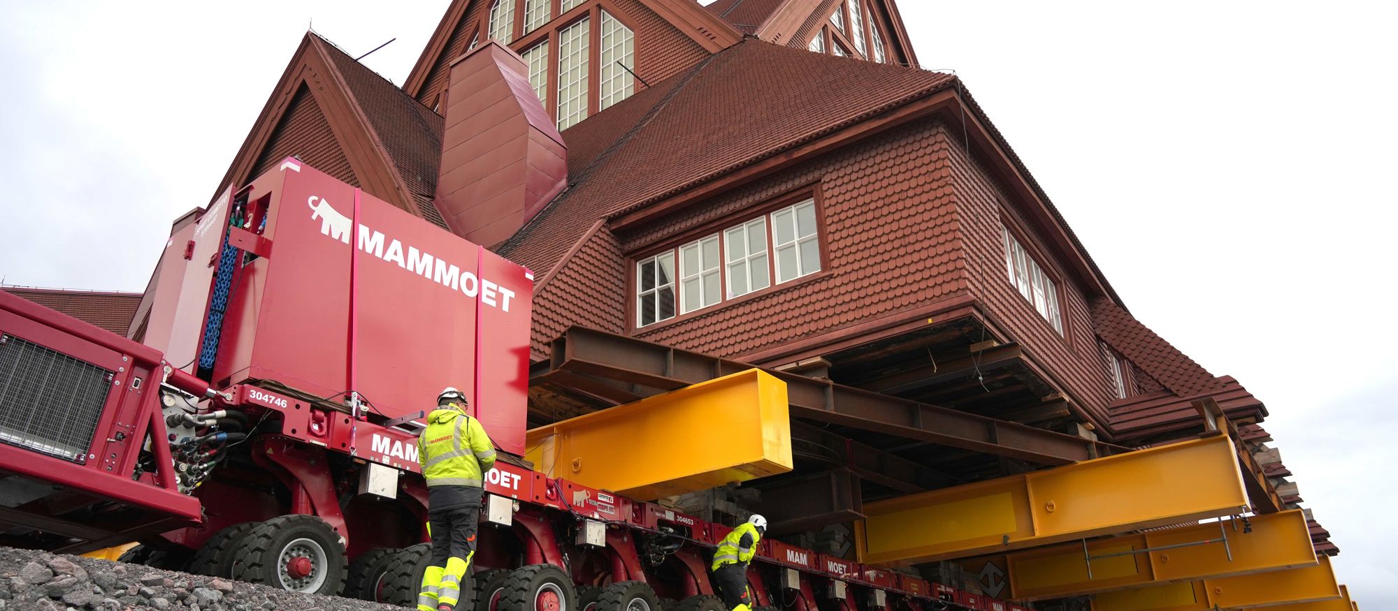 Närbild på en röd träbyggnad uppallrad på en gul trailer som rullar fram - Kiruna kyrka flyttas
