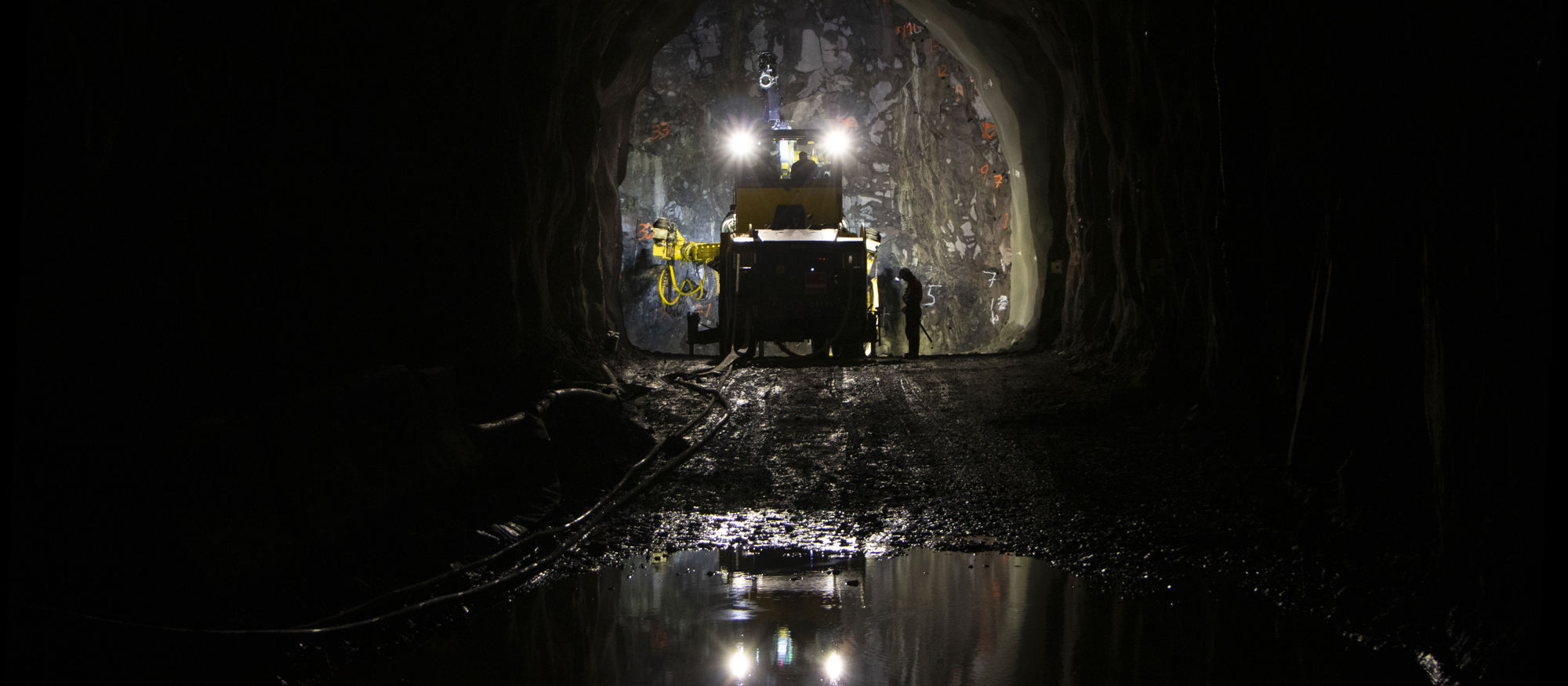 Mörk bild av underjordisk tunnel där en maskin arbetar med strålkastarna på längst in
