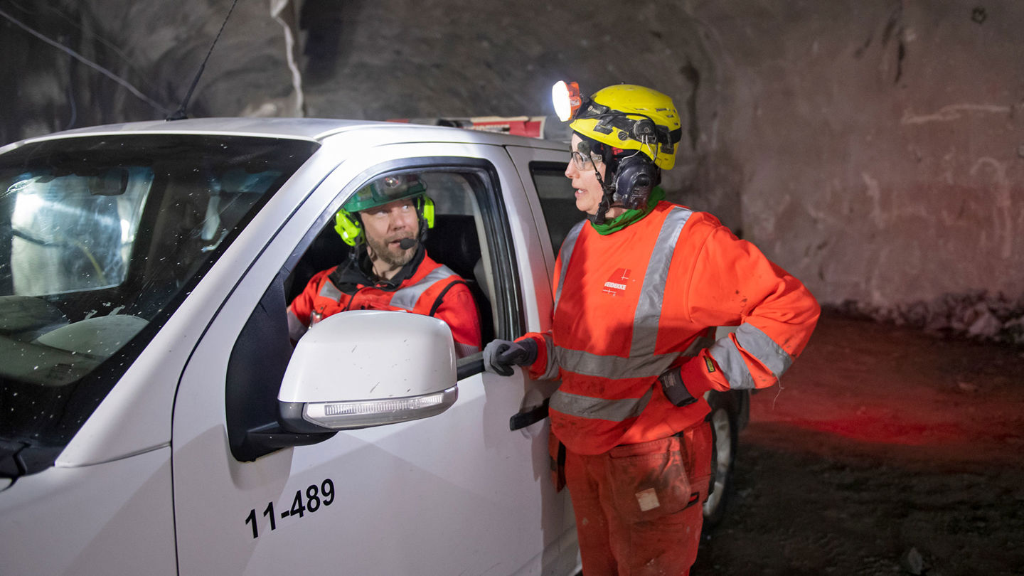 En kvinna står utanför en bil och pratar med mannen som sitter förarsidan.
