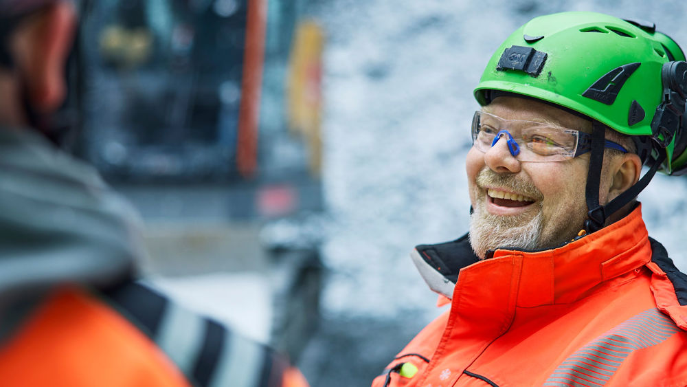 Leende anläggningsarbetare iklädd varseljacka och hjälm.