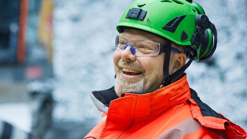 Leende anläggningsarbetare iklädd varseljacka och hjälm.