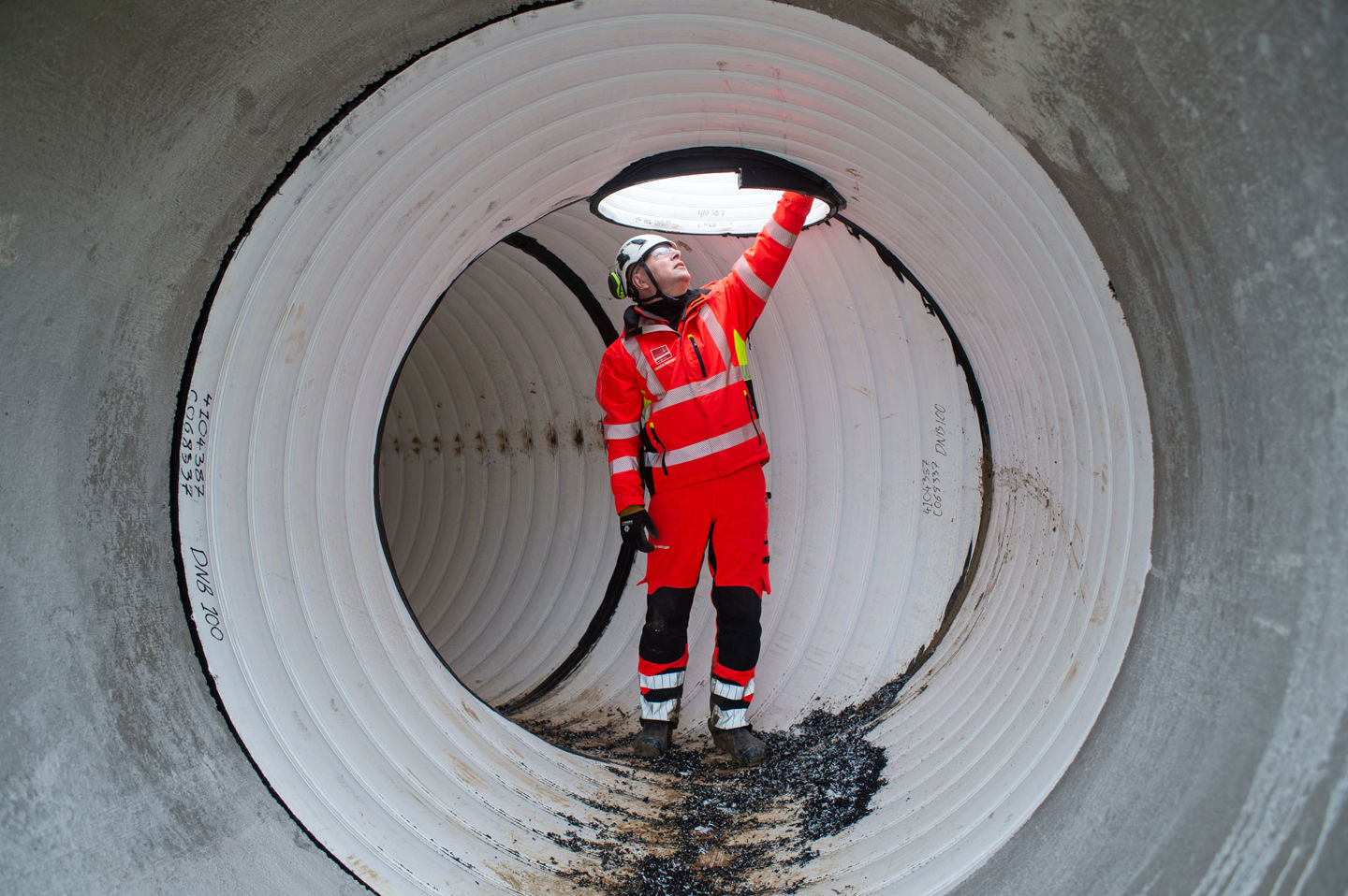 Man i varselkläder och bygghjälm står inne i ett stort rör.