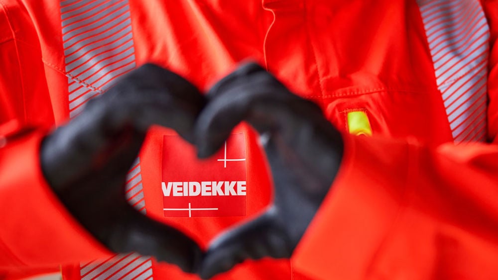 Händer som bildar ett hjärta framför en Veidekke-logo.