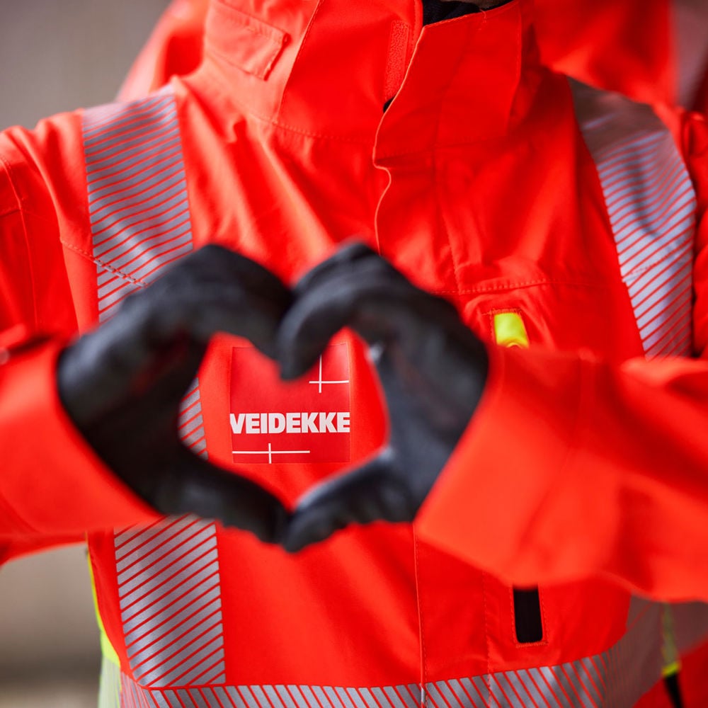 Händer som bildar ett hjärta framför en Veidekke-logo.