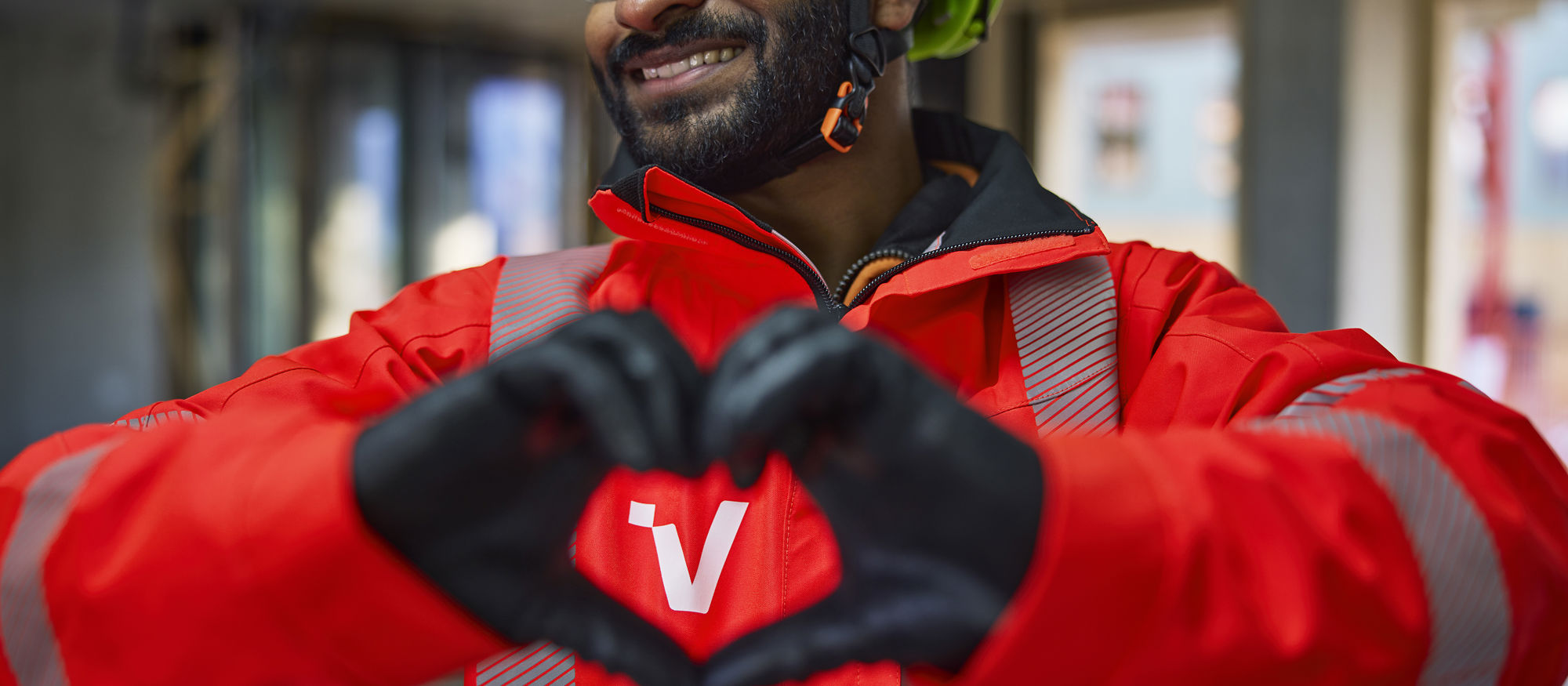 Glad man i varselkläder formar händerna till ett hjärta framför Veidekkes logo på jackan