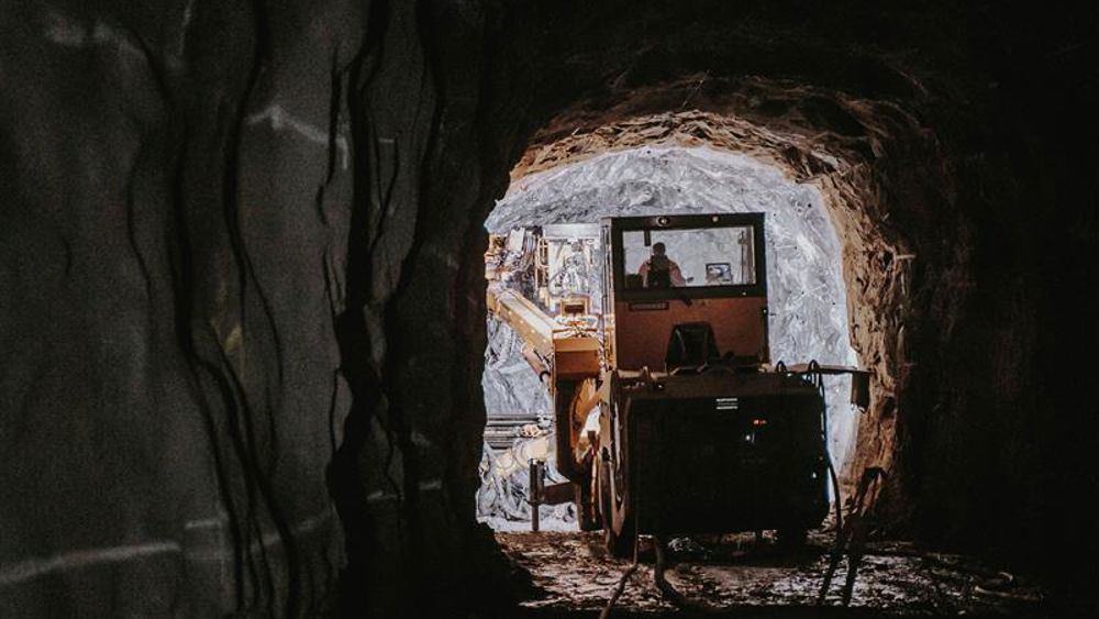 Mörk bergtunnel med anläggningsmaskin i ljuset i mynningen