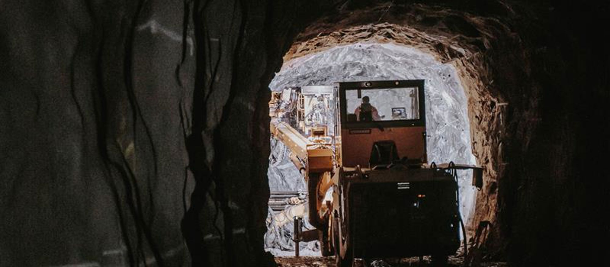Mörk bergtunnel med anläggningsmaskin i ljuset i mynningen