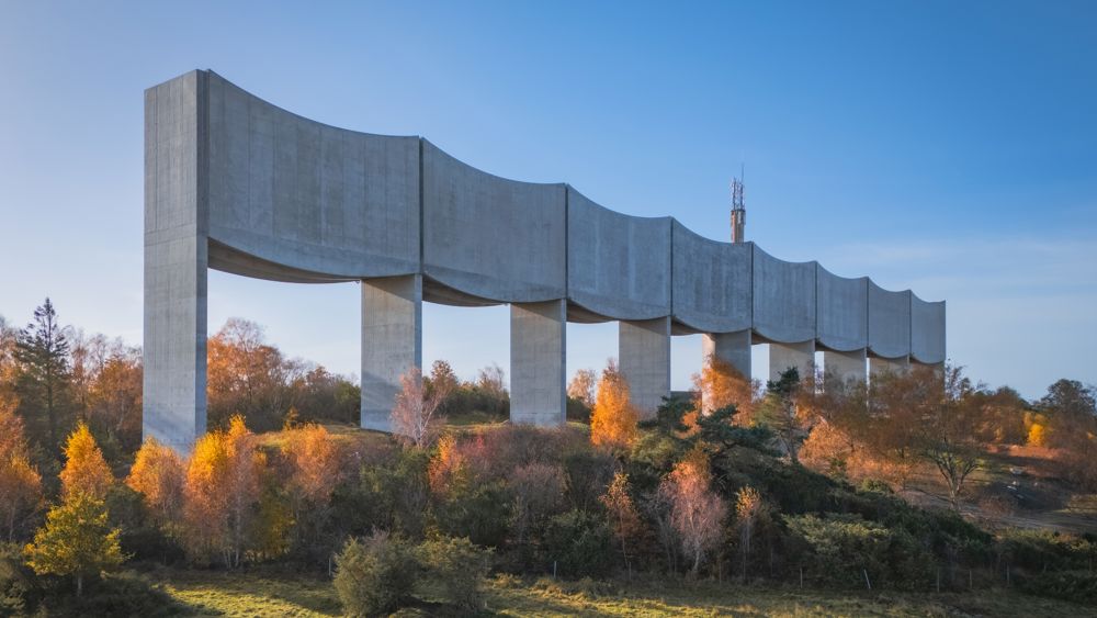 Arkitektbild där Våga vattentorn höjer sig som en våg längs med horisonten. I förgrunden en motorväg framför en bondgård och träd.