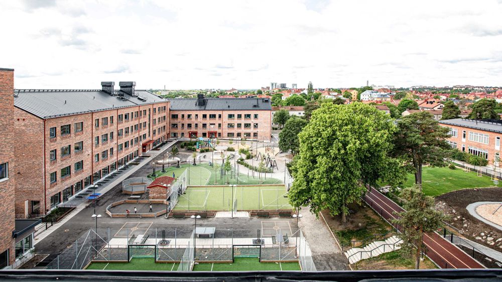 Skolbyggnad i tre våningar  med tegelfasad breder ut sig som ett "L" runt en skolgård