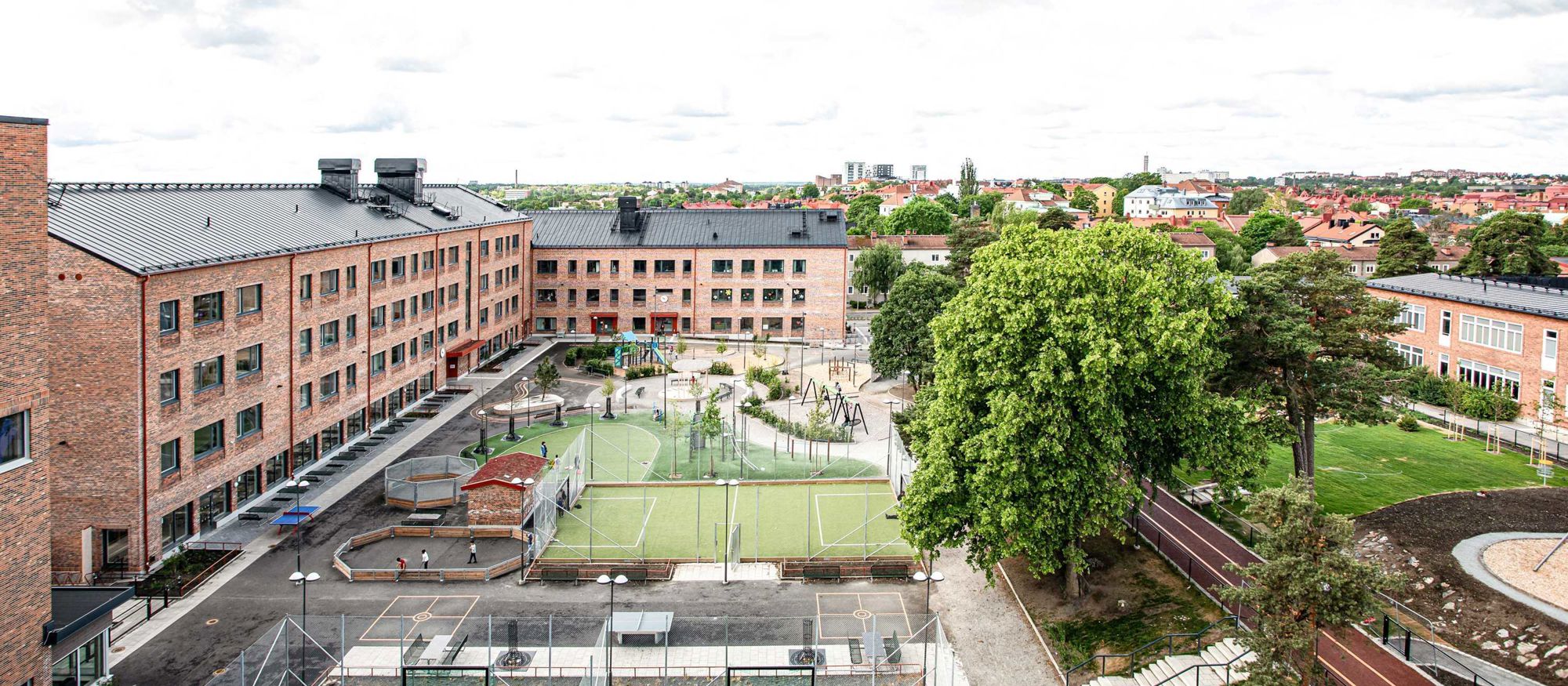 Skolbyggnad i tre våningar  med tegelfasad breder ut sig som ett "L" runt en skolgård