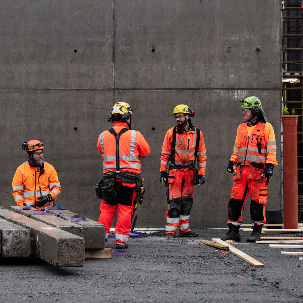 Fyra män står i varselkläder framför en betongvägg