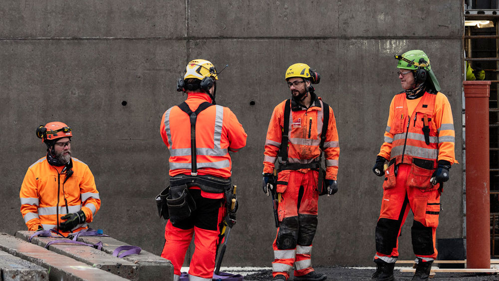 Fyra män står i varselkläder framför en betongvägg
