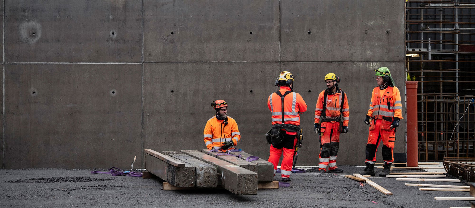 Fyra män står i varselkläder framför en betongvägg