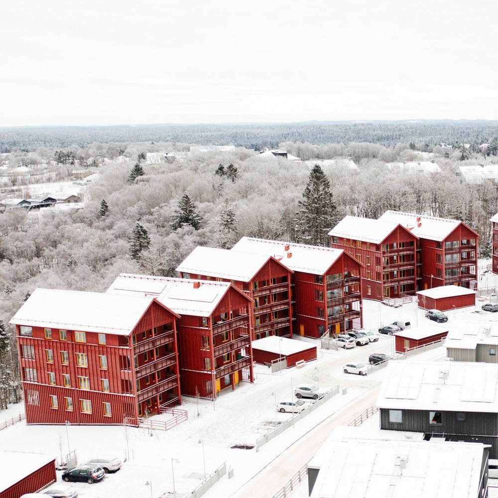 Röda lägenhetshus i trä i vintervitt landskap.