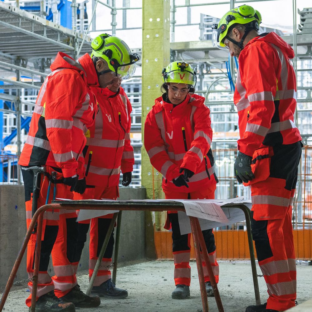 Ett team i varselkläder samlas runt en ritning i ett byggprojekt