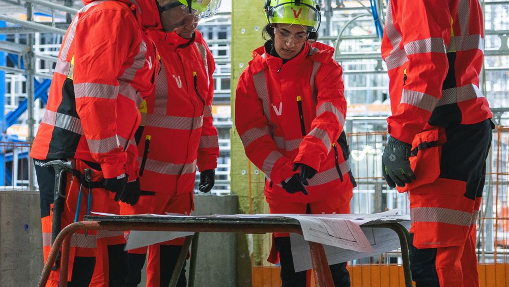 Ett team i varselkläder samlas runt en ritning i ett byggprojekt