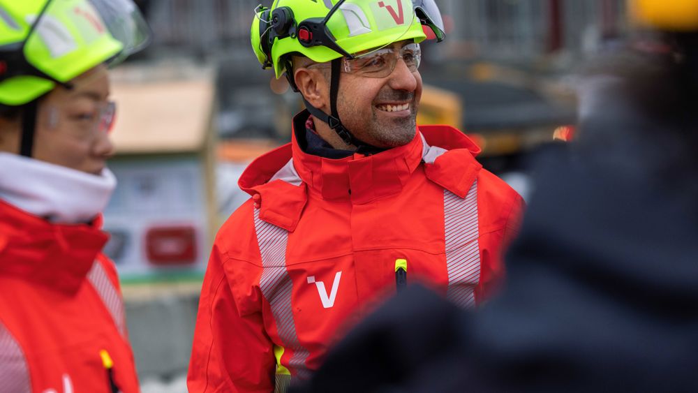 Halvfigursbild av två personer i gula hjälmar och Veidekkes röda varselkläder