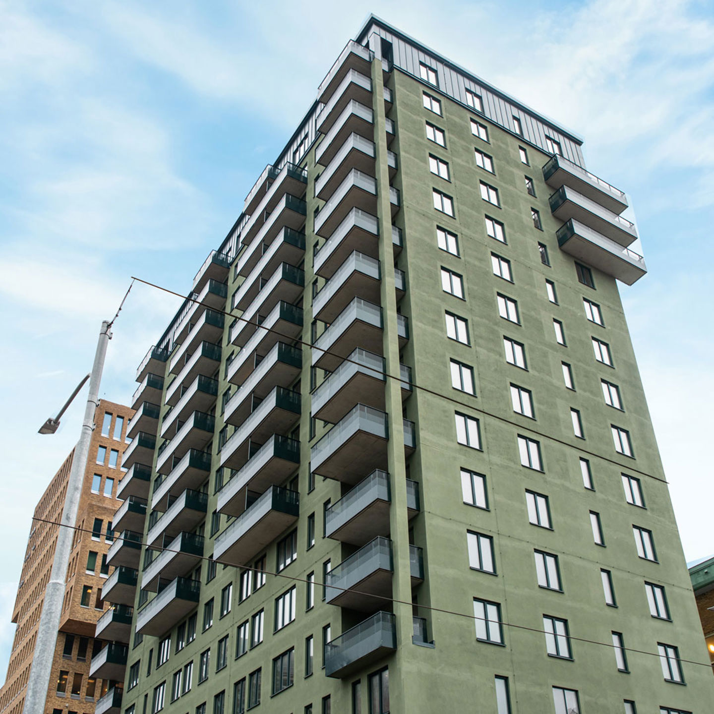 Cicerons gröna putsfasad reser sig mot himlen. Bostadshus i cirka 15 våningar med ljusa balkonger.