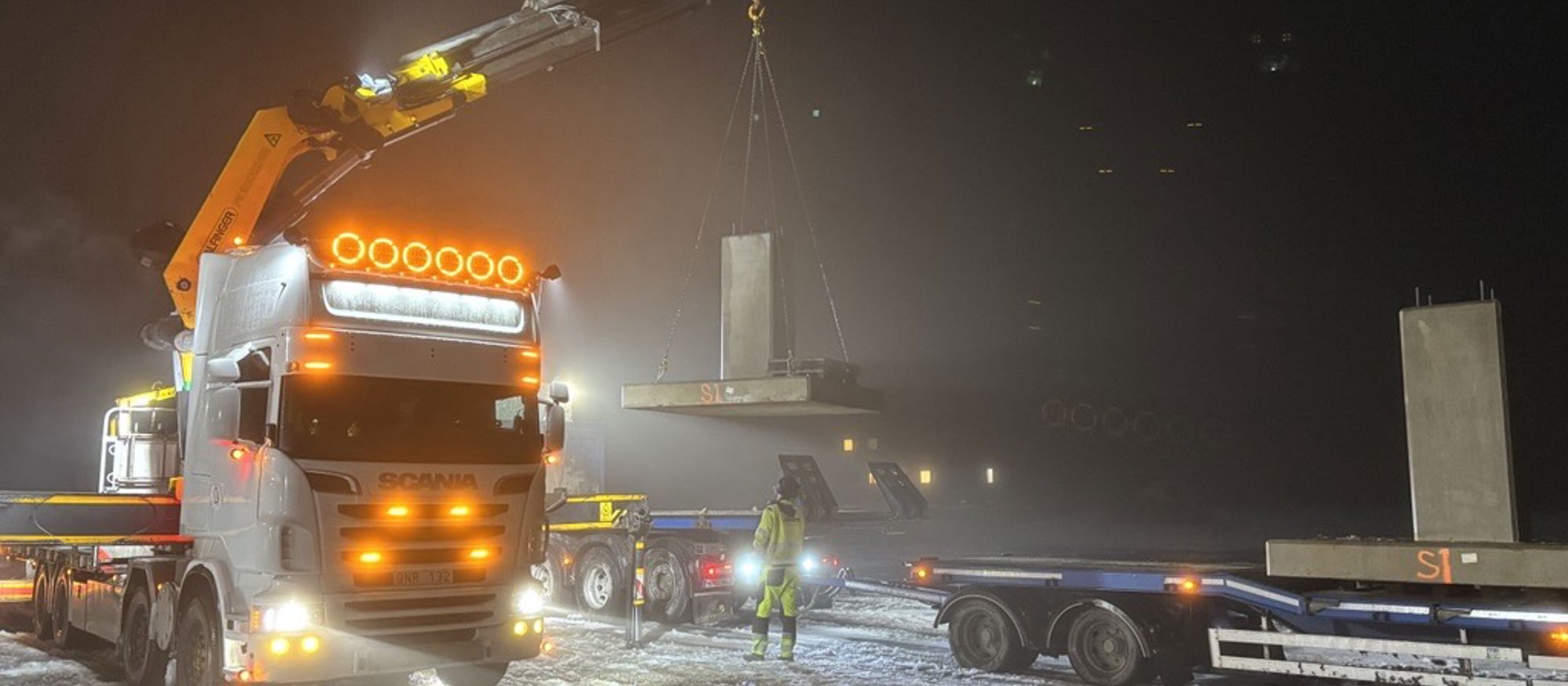 Lastbil i i mörkt vinterlandskap lyfter ett betongfundament