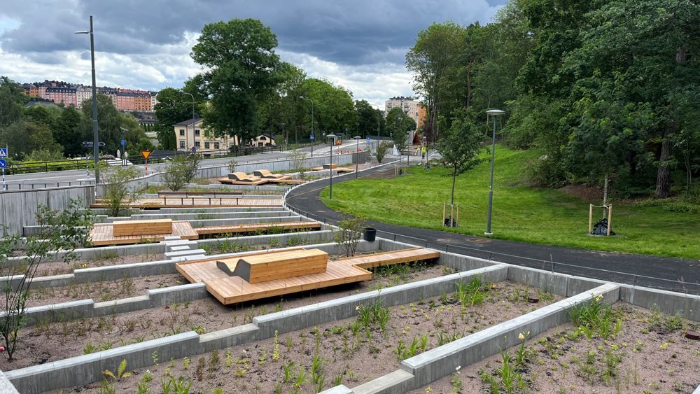 Nyanlagd offentlig utomhusmiljö med gräsmatta, cykelvägar och sittbänkar i en sluttning