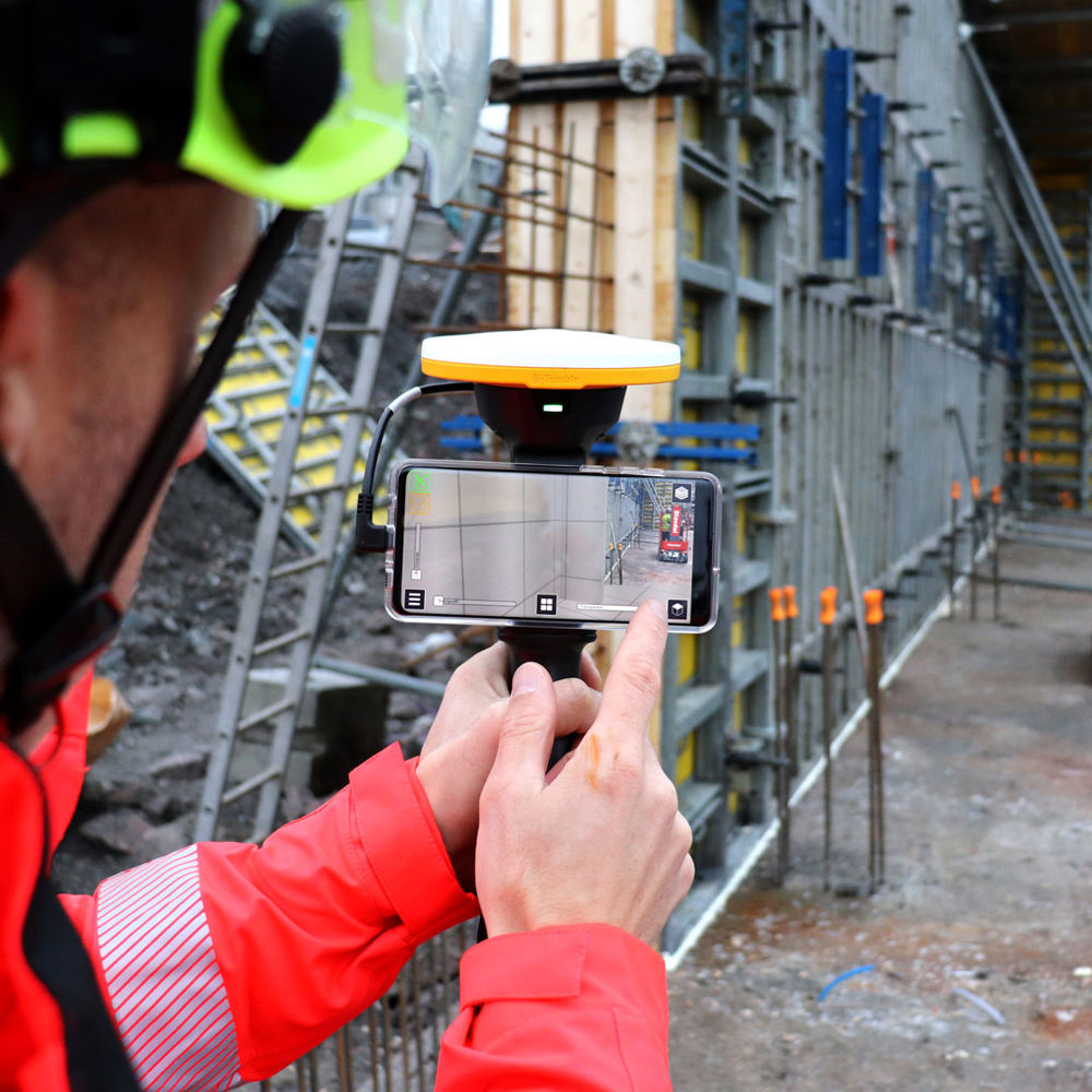 Person står och mäter genom en mobiltelefon på en byggarbetsplats.