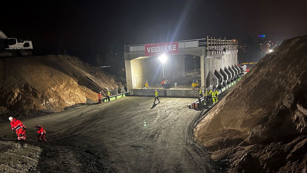 Brodalsmotet. Mörkebild där strålkastare lyser upp ett vägprojekt med stora maskiner. En vägport i betong syns i mitten, änne helt fristående på marken. 