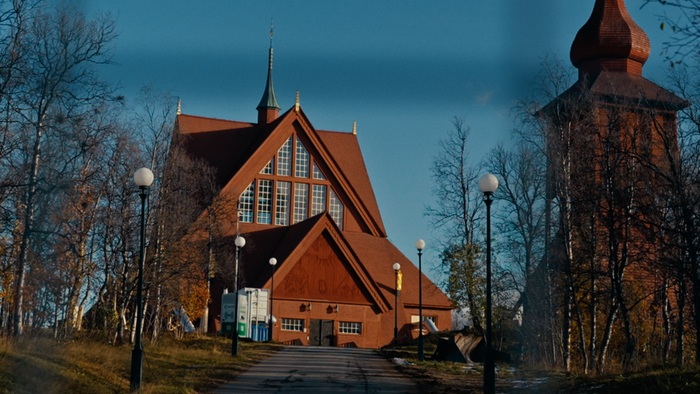 Thumbnail-bild från film om flytten av Kiruna kyrka. Här syns den röda kyrkan med sin klockstapel på en kulle i slutet av en gångväg.