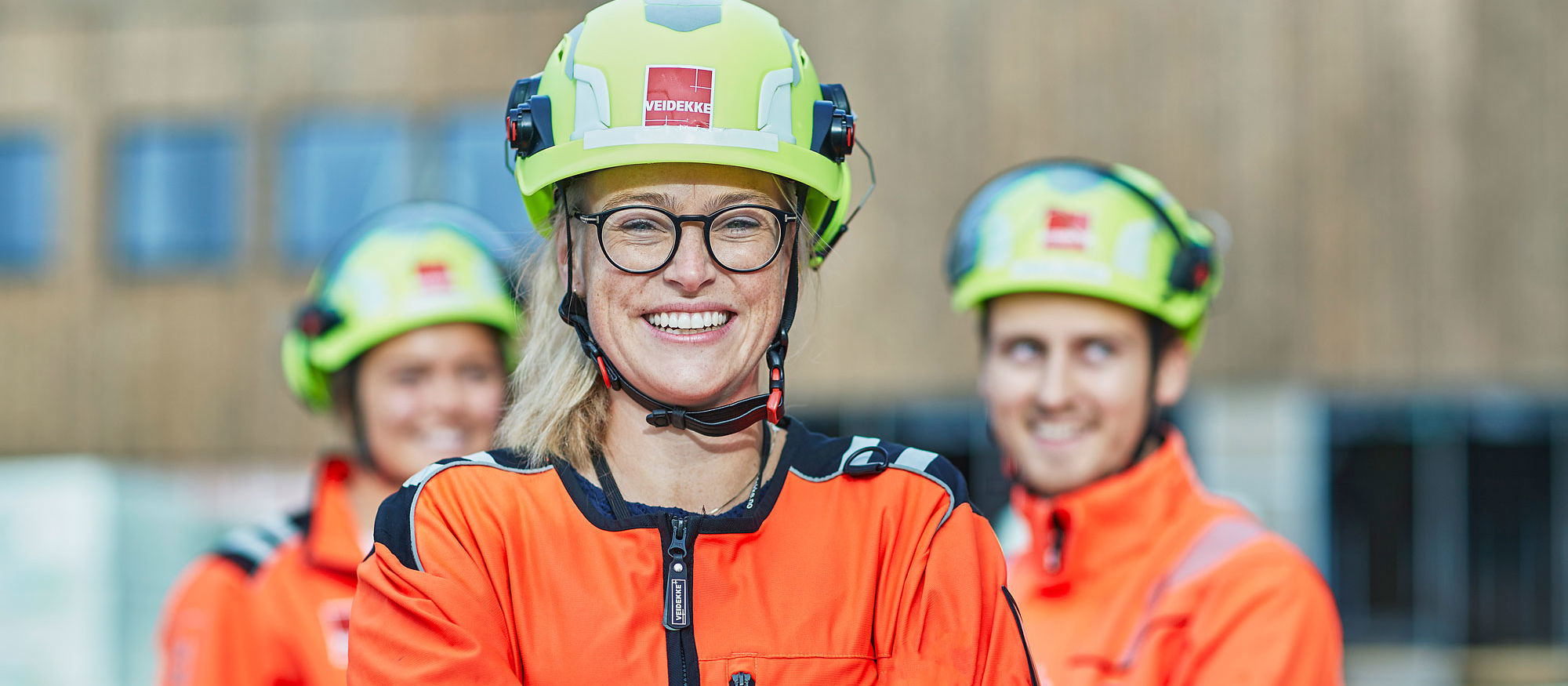 En tjej i varselkläder står leende med två kollegor i bakgrunden.