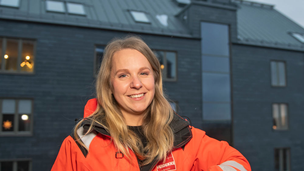 Foto av en medarbetar på Veidekke stående framför ett skifferhus.