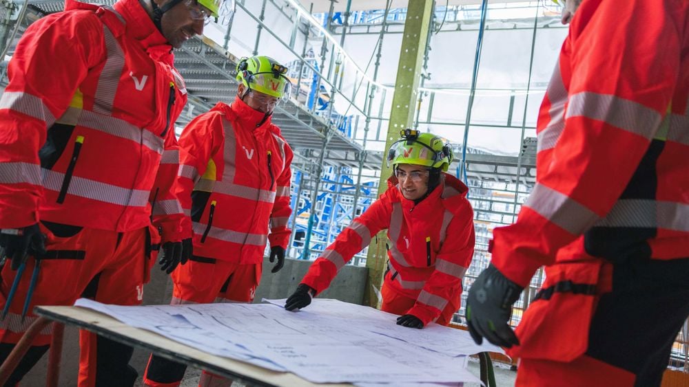 En grupp byggnadsarbetare i varselkläder samlade runt en ritning ute i ett projekt