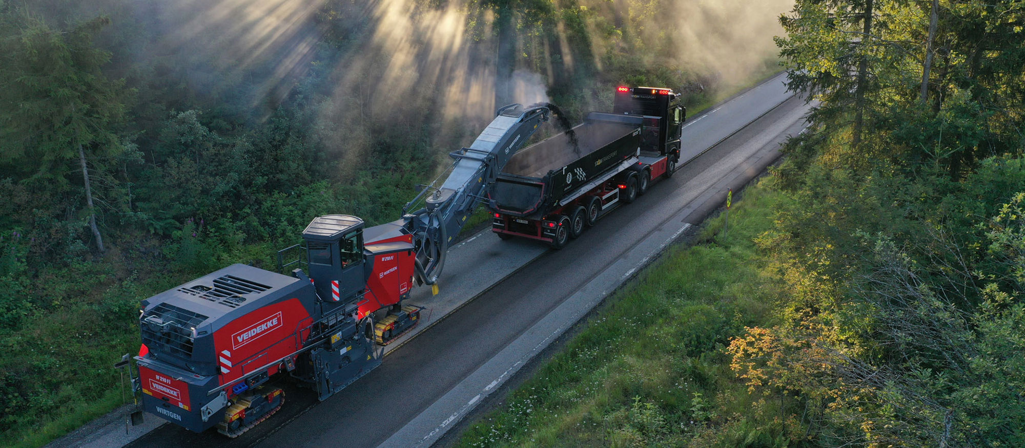 Asfaltutläggning på en väg genom en skog.