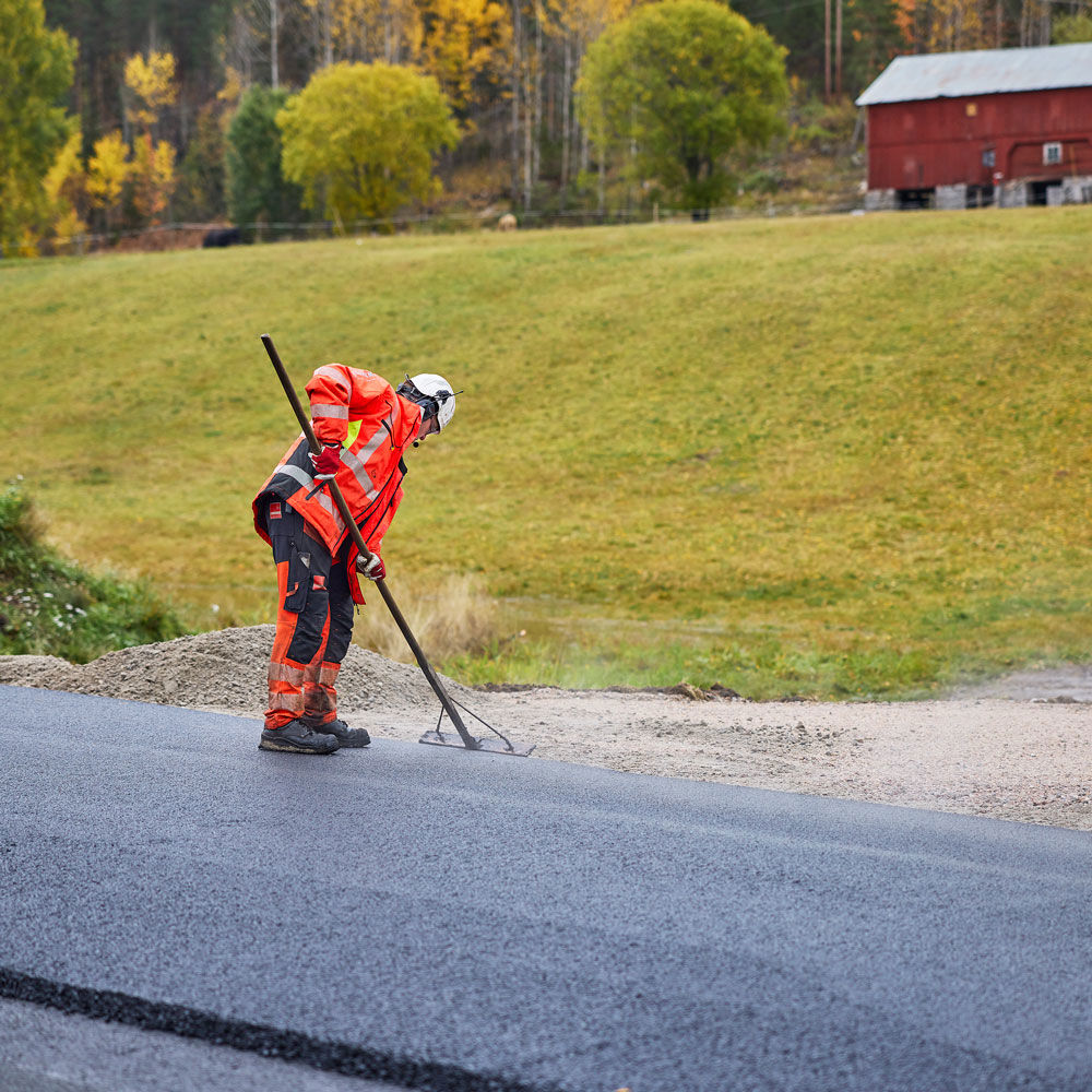 Man som asfalterar en väg med gräs i bakgrunden.