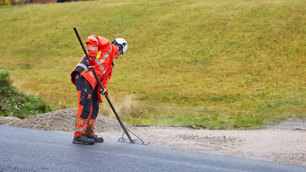Man som asfalterar en väg med gräs i bakgrunden.