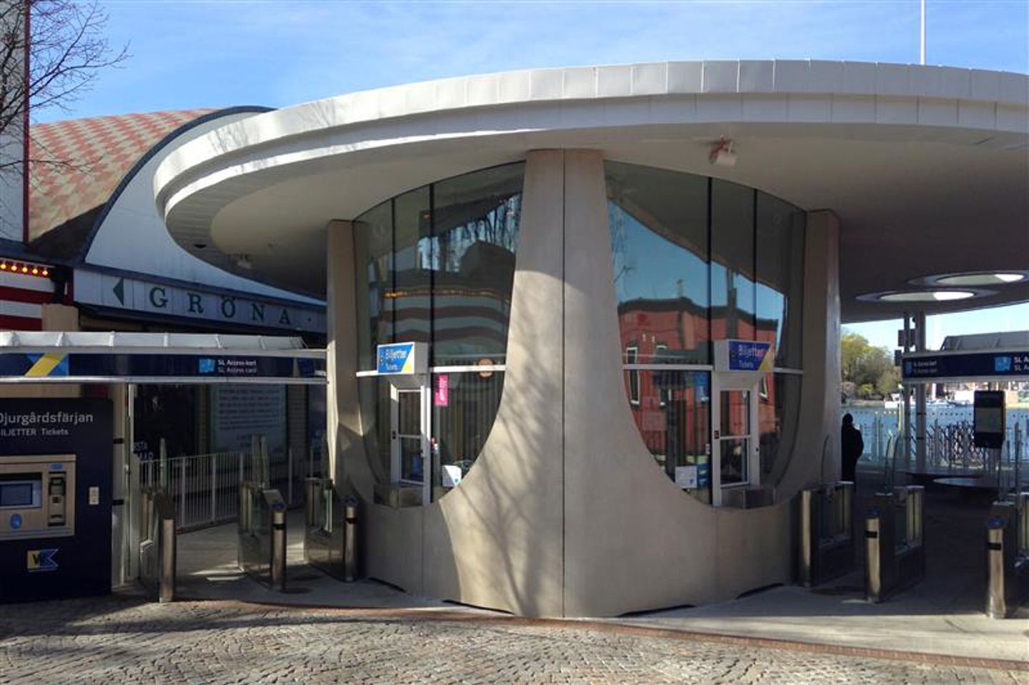Biljettkur för färja vid Gröna lund. Grå betongbyggnad i grått med utskjutande tak och glaspaneler. 