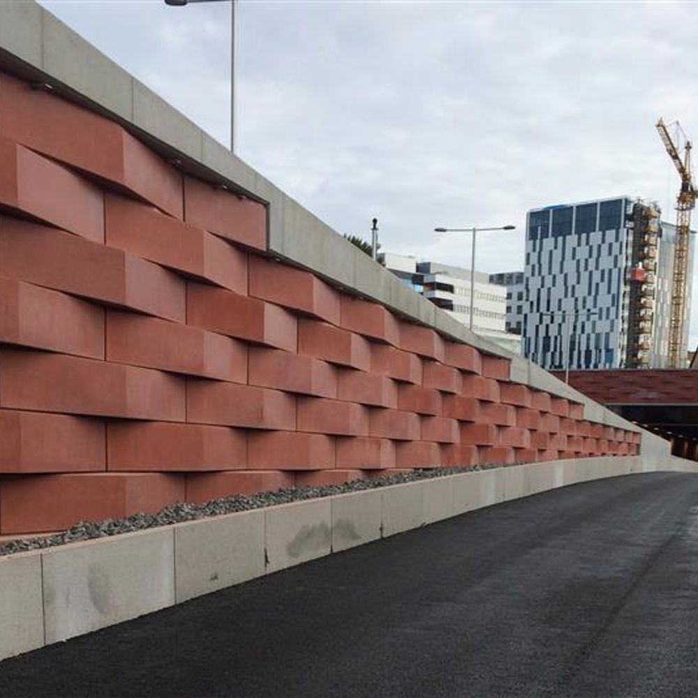 Konstfärdigt utförd mur i terrakottafärgad betong vid motorväg. Höghus och byggkran i bakgrunden. 