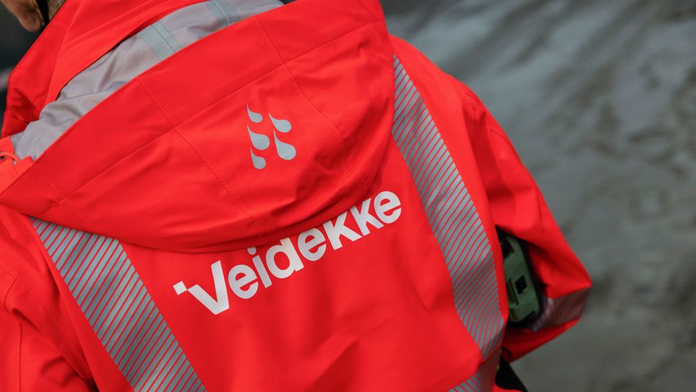 Ryggen på en person som bär Veidekkes orange arbetskläder med logga