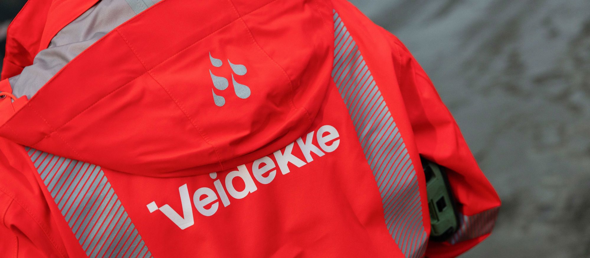Ryggen på en person som bär Veidekkes orange arbetskläder med logga