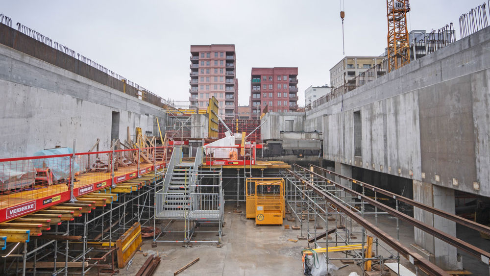 Byggarbetsplats under marknivå där man ser bostadshus i bakgrunden ovan marknivå.