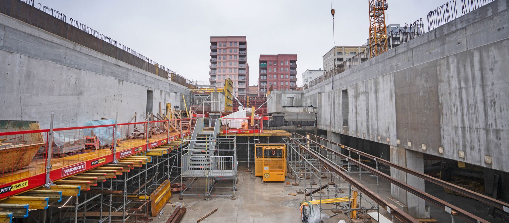 Byggarbetsplats under marknivå där man ser bostadshus i bakgrunden ovan marknivå.