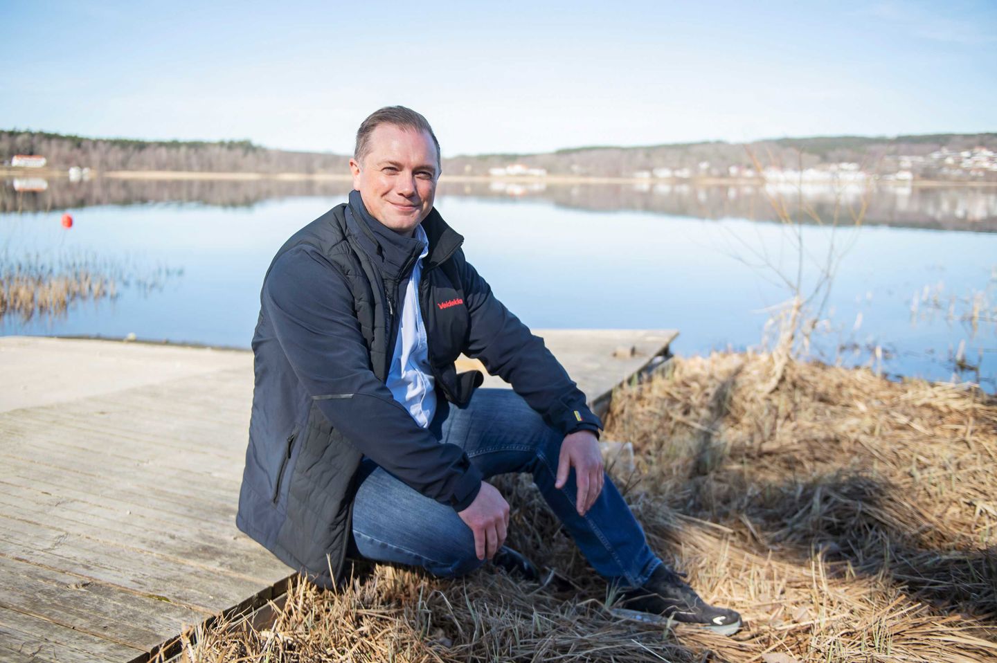 En leende man, Marcus Dahlberg, sitter på en brygga med en lugn sjö i bakgrunden