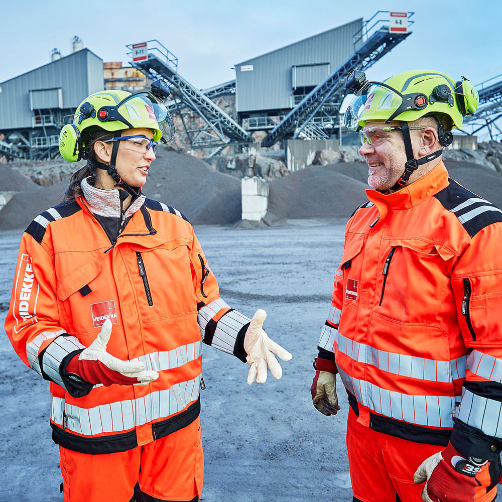Två människor i bygghjälm och varselkläder diskuterar.